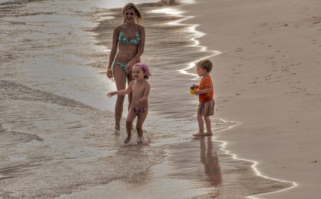 A mother and two young children playing at the water's edge on a beach in Punta Cana