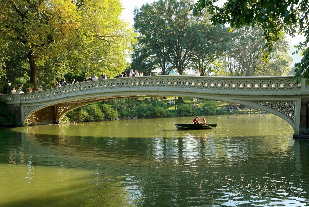 Bow Bridge crossing the Lake in Central Park with trees and Manhattan buildings behind