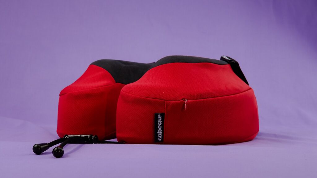 A red memory foam travel neck pillow with seat straps on a purple background