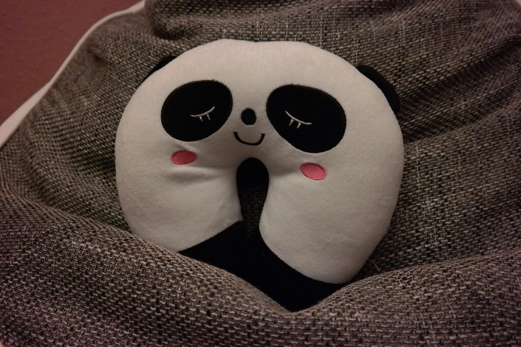 A soft panda-shaped travel neck pillow resting on a fabric seat