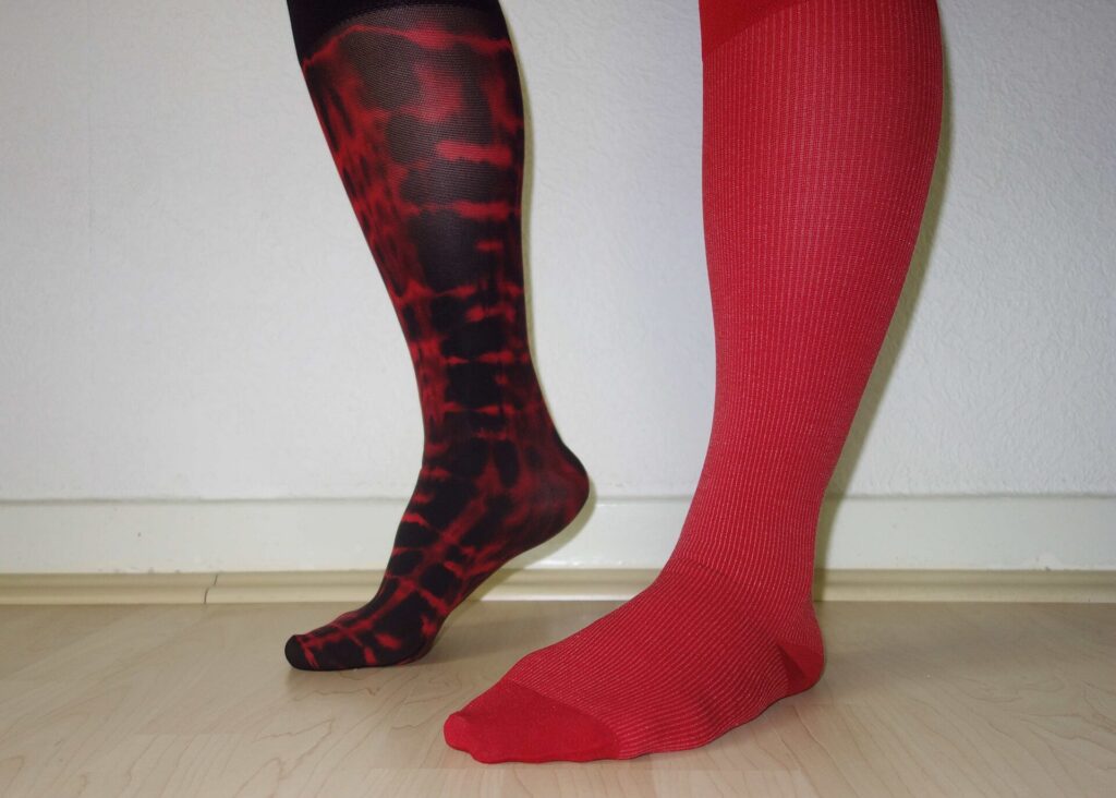 Two legs wearing knee-high compression socks, one patterned and one plain red
