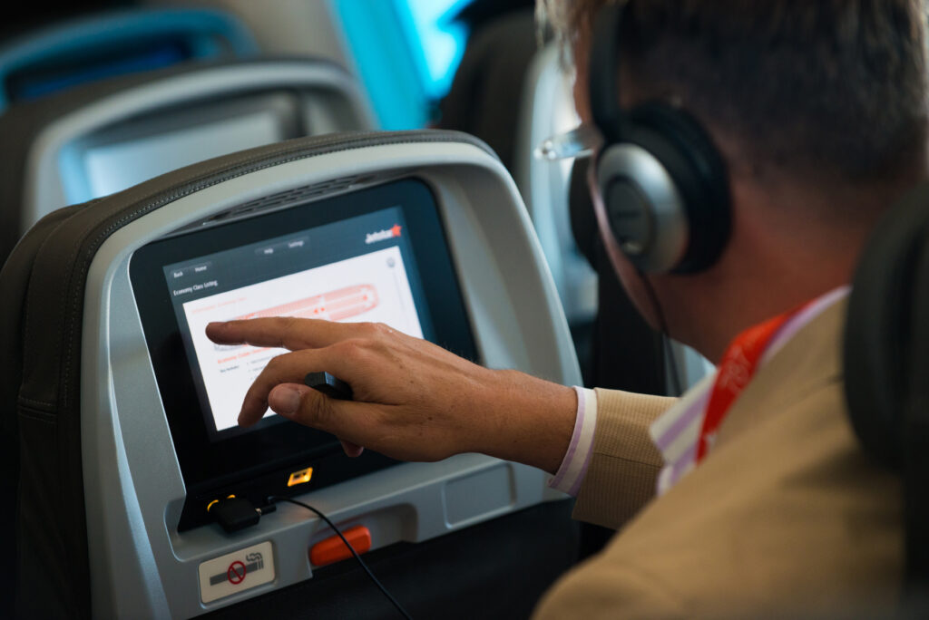 A passenger wearing headphones using a seatback entertainment screen in an economy cabin