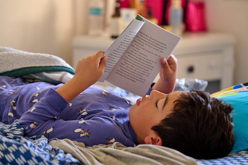 A boy lying down and reading a chapter book