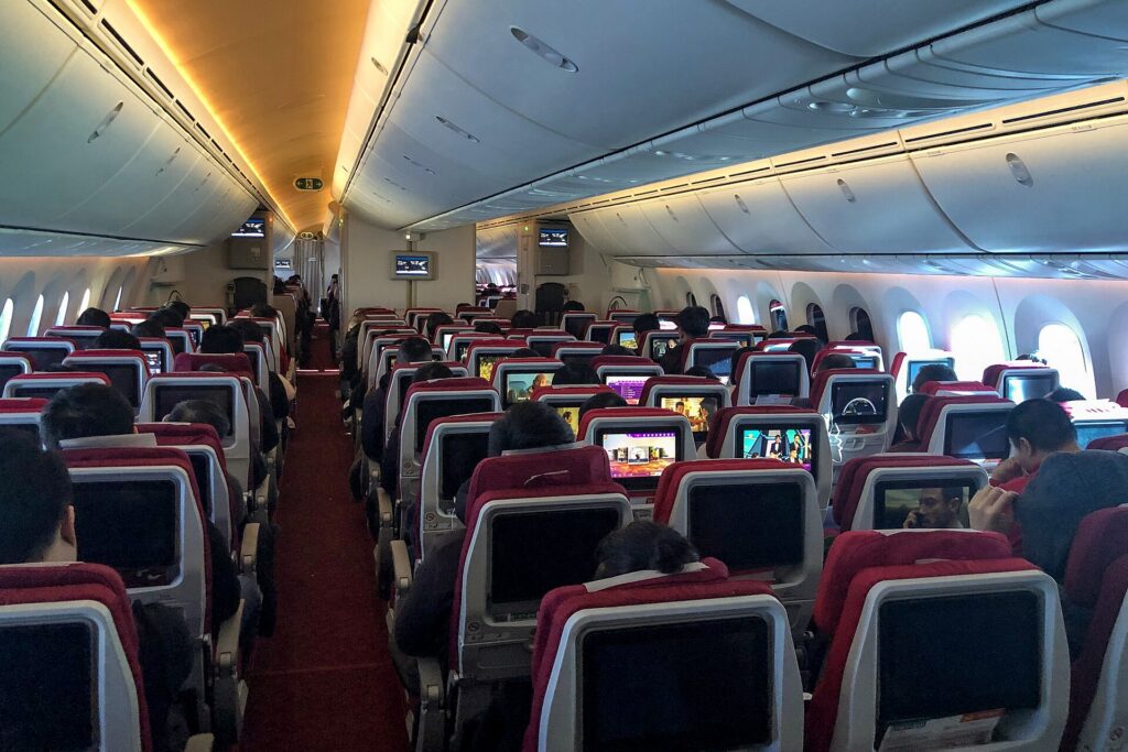 The economy cabin of a widebody airliner with rows of seats and seatback screens