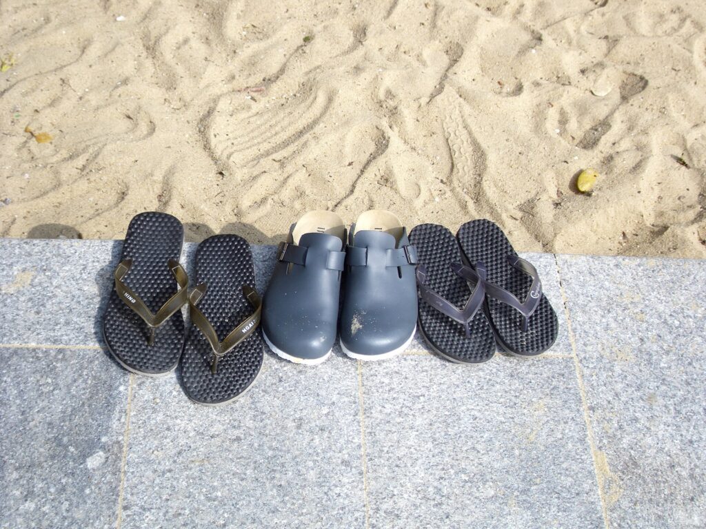 Black flip-flops and leather sandals side by side on a beach