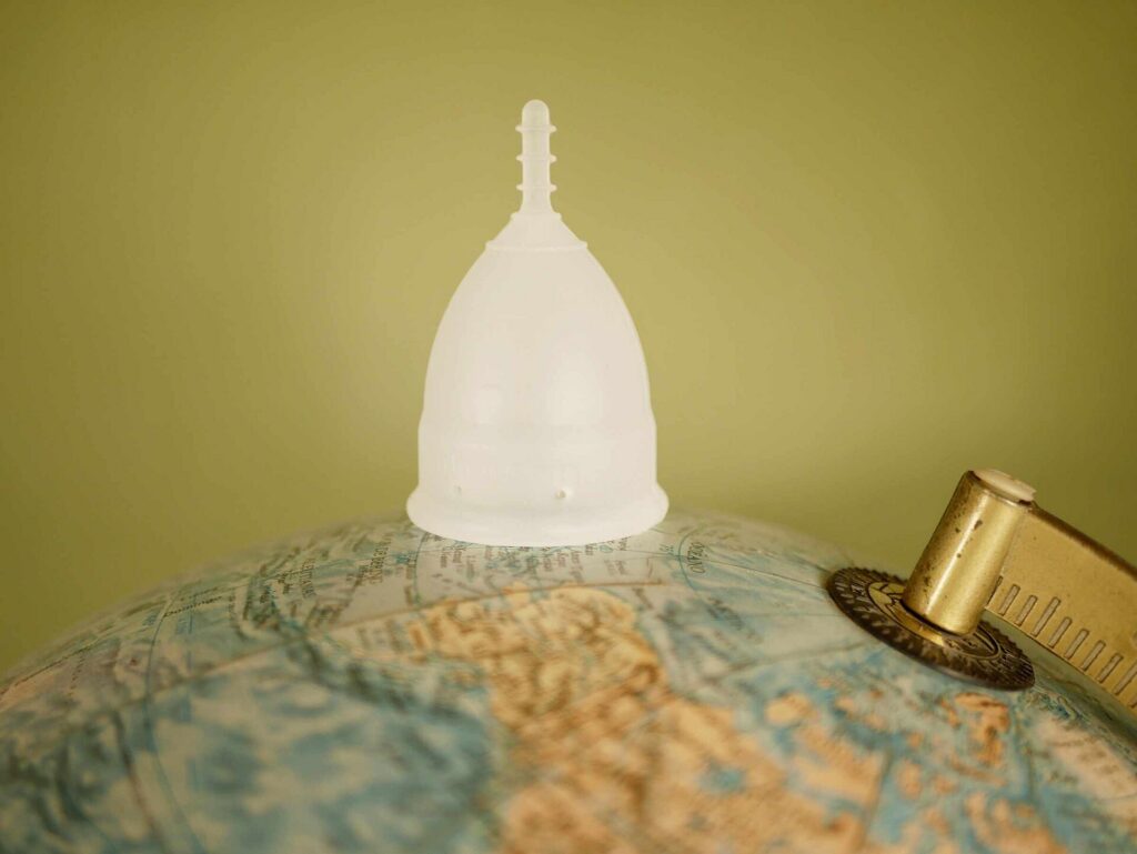 A reusable menstrual cup placed next to a small world globe