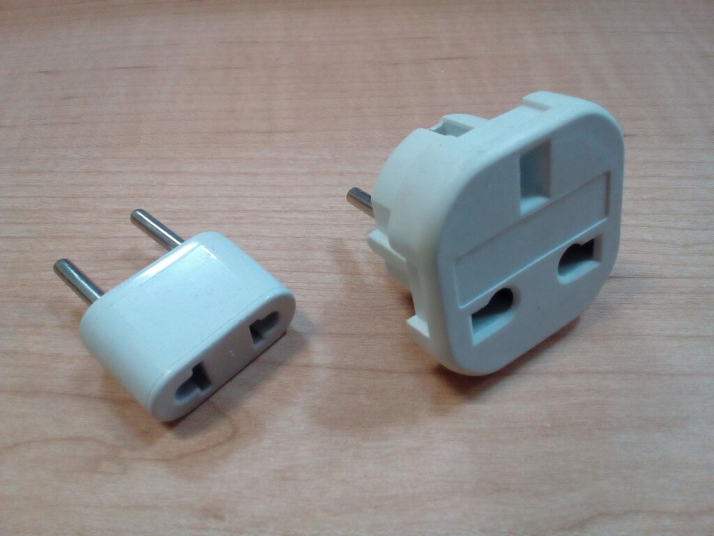 Two plug adapters for different electrical outlet types on a wooden table