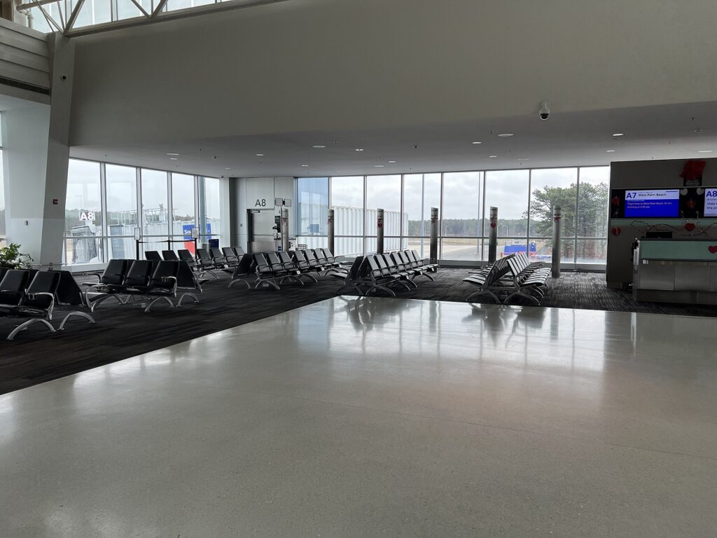 Rows of seats in an airport gate area with large windows onto the airfield