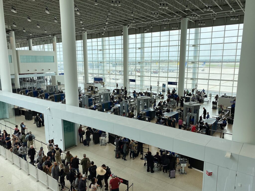 Passengers lined up at a TSA security checkpoint in a bright airport terminal