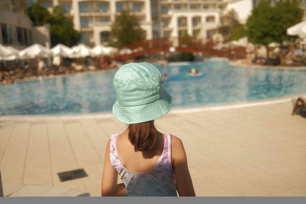 A young child in a sun hat standing beside a resort swimming pool