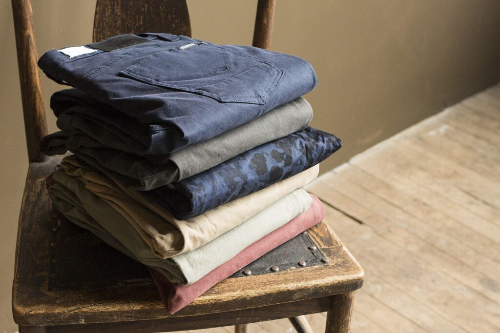 A stack of folded chino pants in different colors on a chair