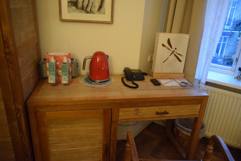 A wooden writing desk with a phone and kettle in a hotel room