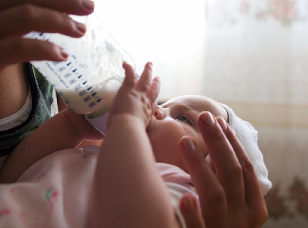 A baby drinking milk from a bottle held by a parent