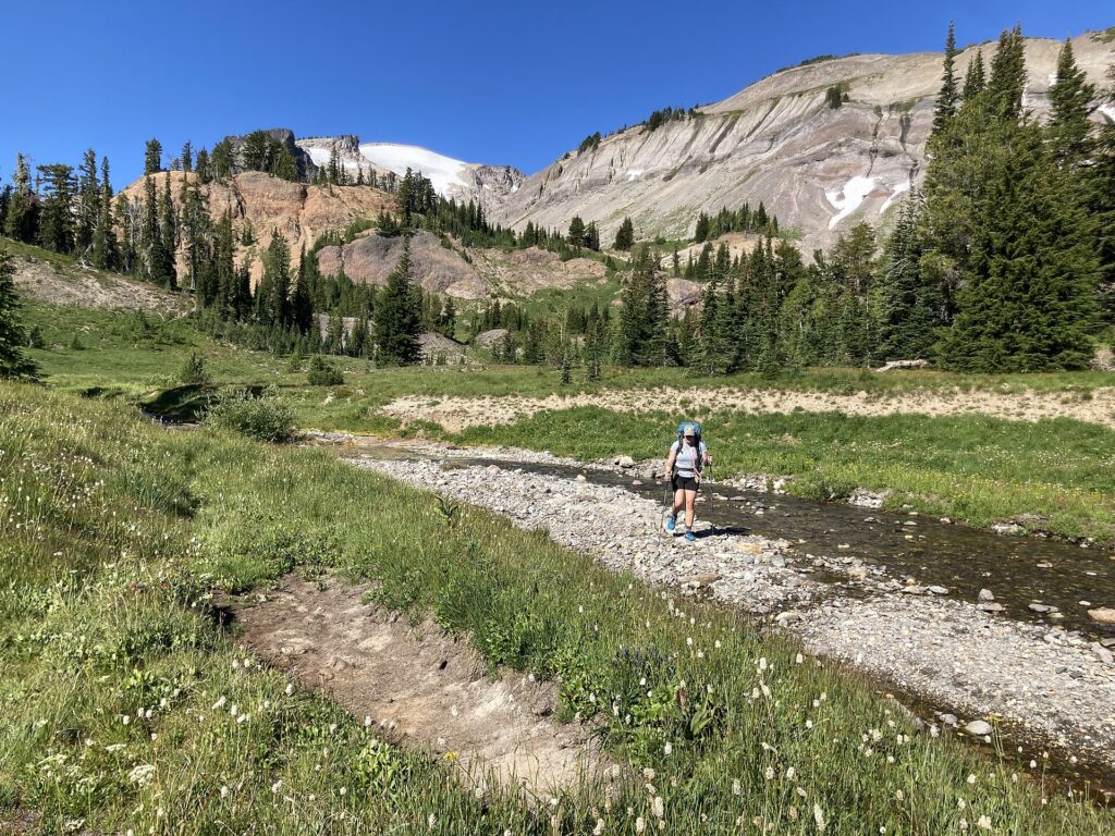 A backpacker with a loaded pack crossing a mountain stream