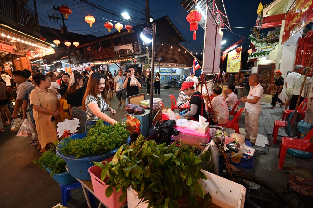 A crowded evening market with shoppers browsing food stalls under lanterns