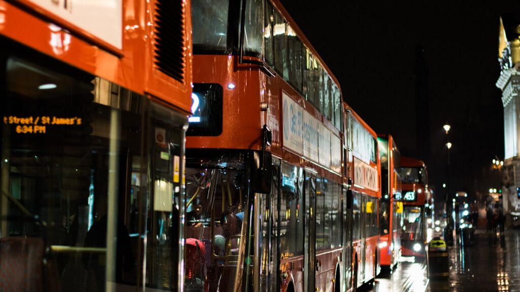 A red double-decker bus on a London street at night